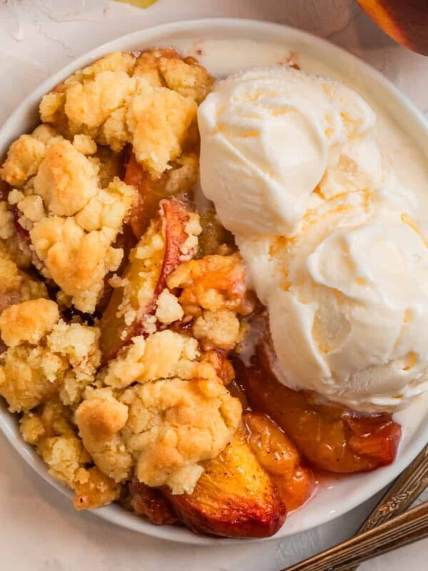 Overhead view of peach cobbler with cake mix on white plate with two scoops of vanilla ice cream.