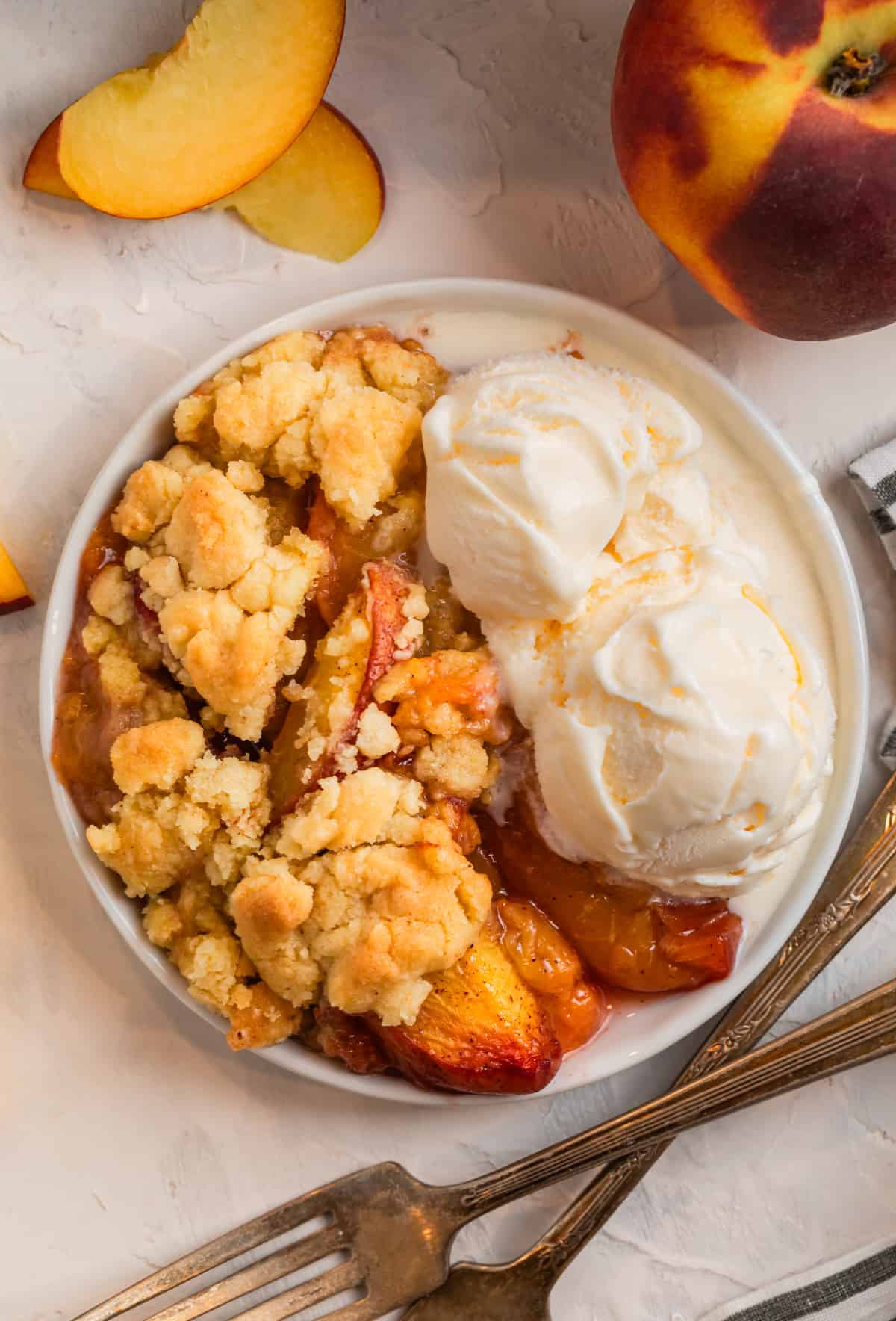 Peach cobbler made with cake mix on white plate with vanilla ice cream scoops.