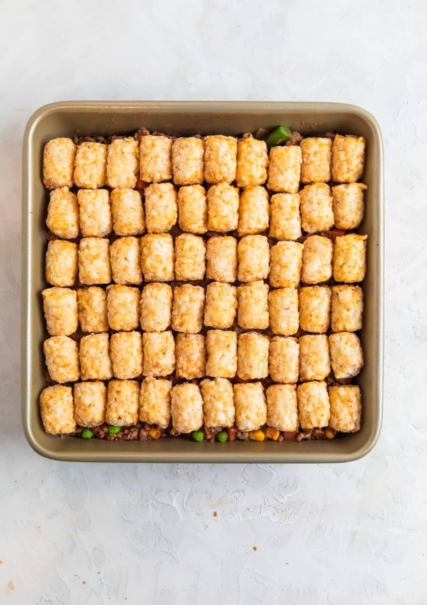 Tater tots lined over beef mixture in baking pan.