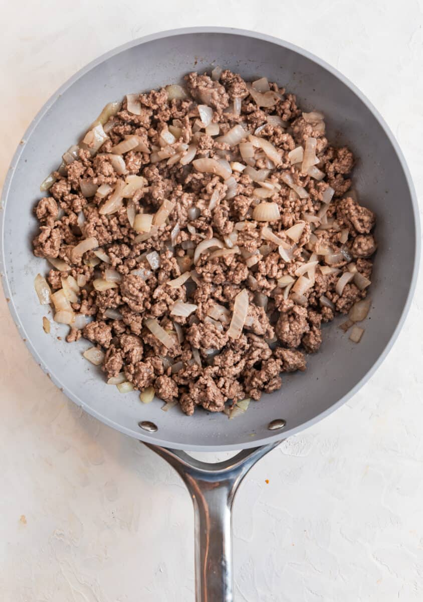 Ground beef and onions cooked in gray skillet.