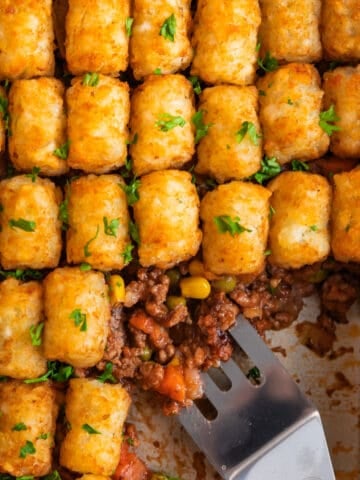Pan with tater tot shepherds pie with serving utensil scooping in.