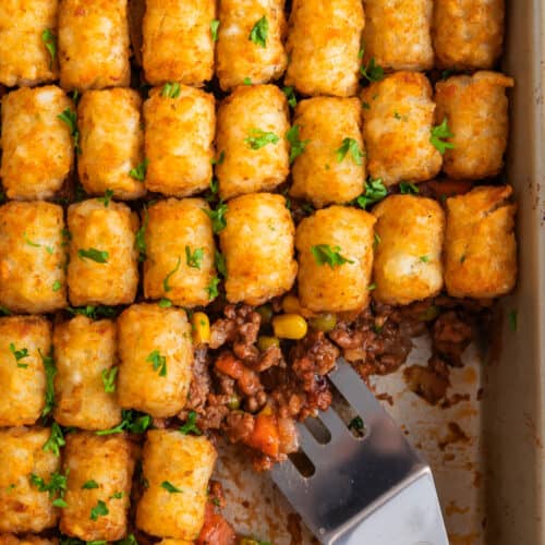 Pan with tater tot shepherds pie with serving utensil scooping in.