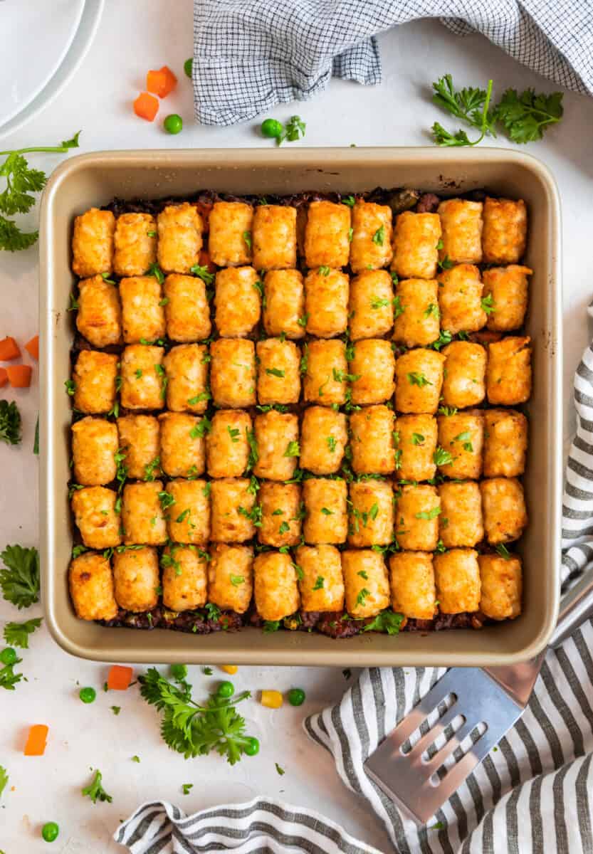 Baked tater tot shepherd's pie in pan with spatula and napkin beside.