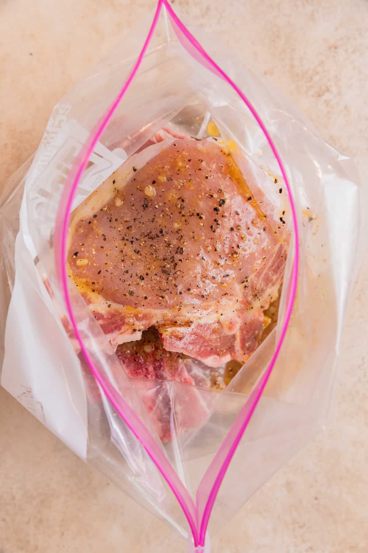 Raw pork chops in plastic bag with lemon pepper marinade over top.