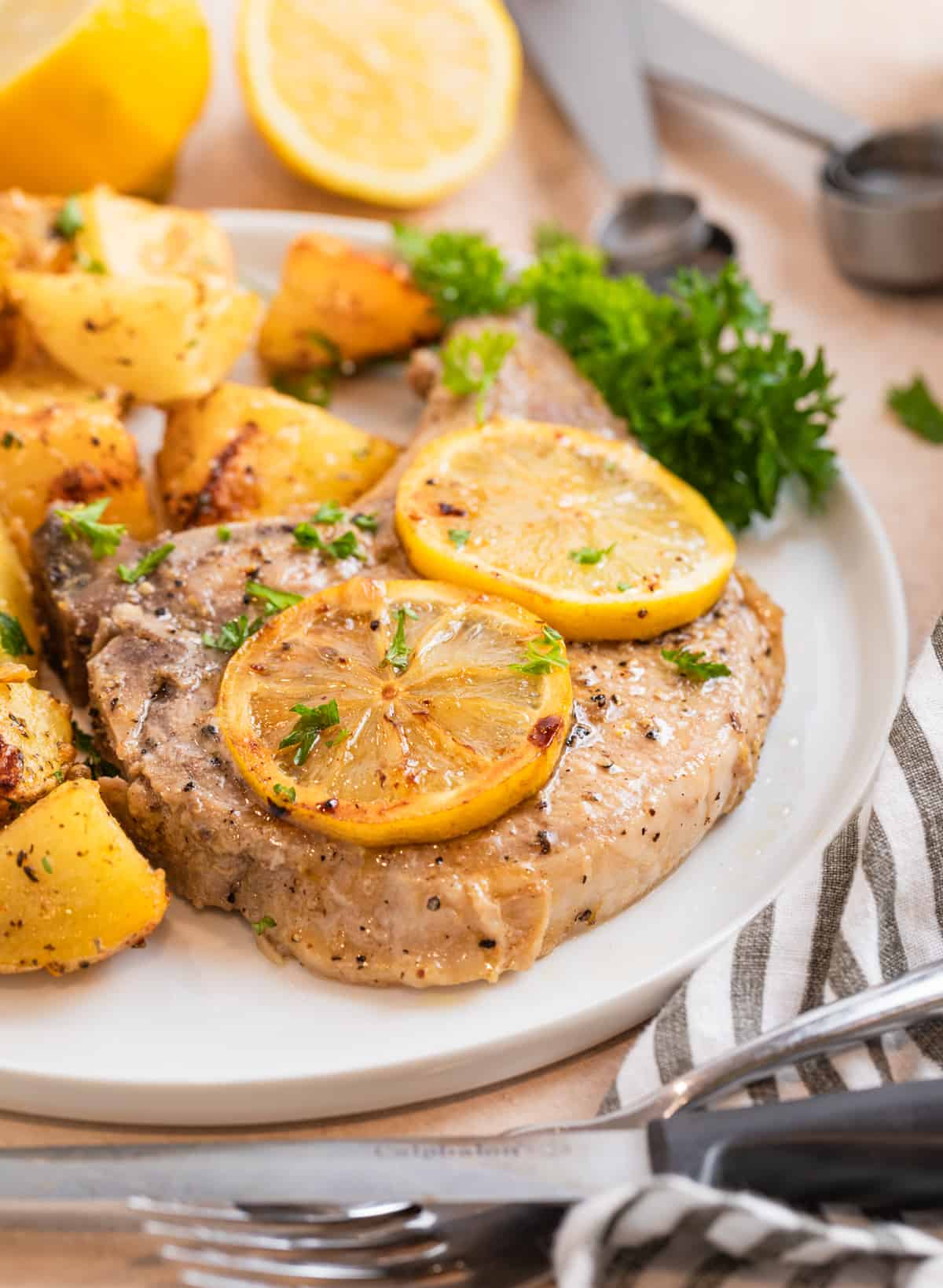 Pork chop and potatoes on white plate with parsley and sliced lemons over top.