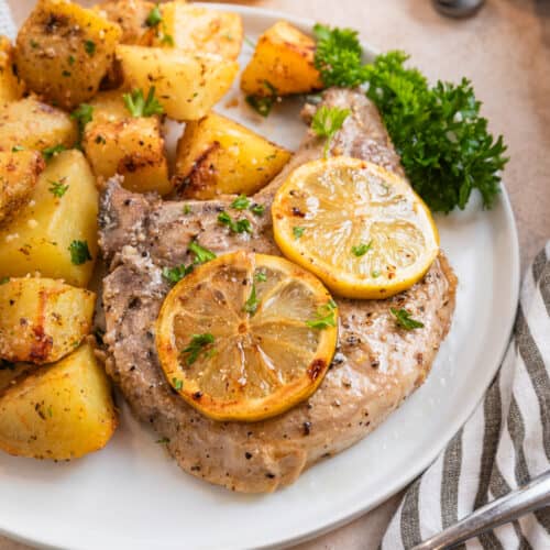 Lemon pepper pork chop on white plate with lemon slices and freshly chopped parsley.