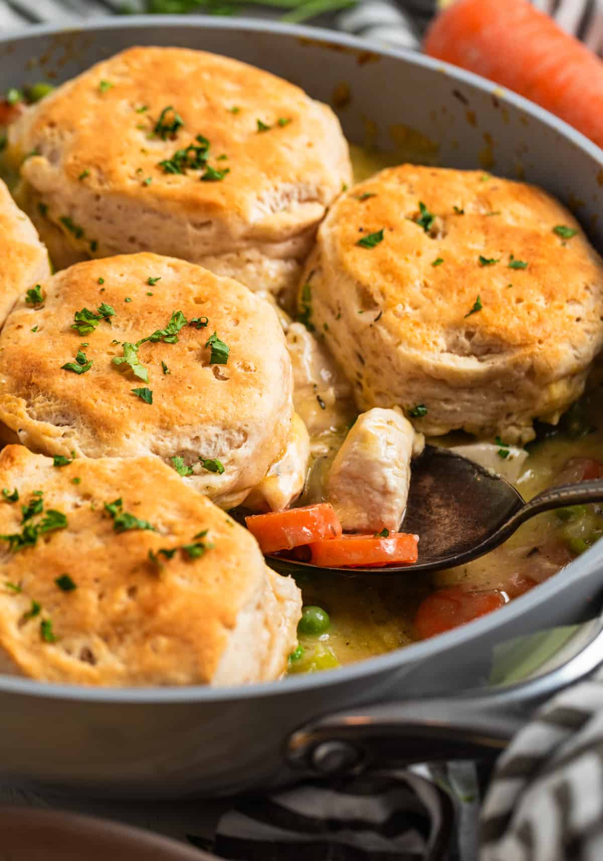 Skillet with chicken and biscuits and serving spoon scooping into it.