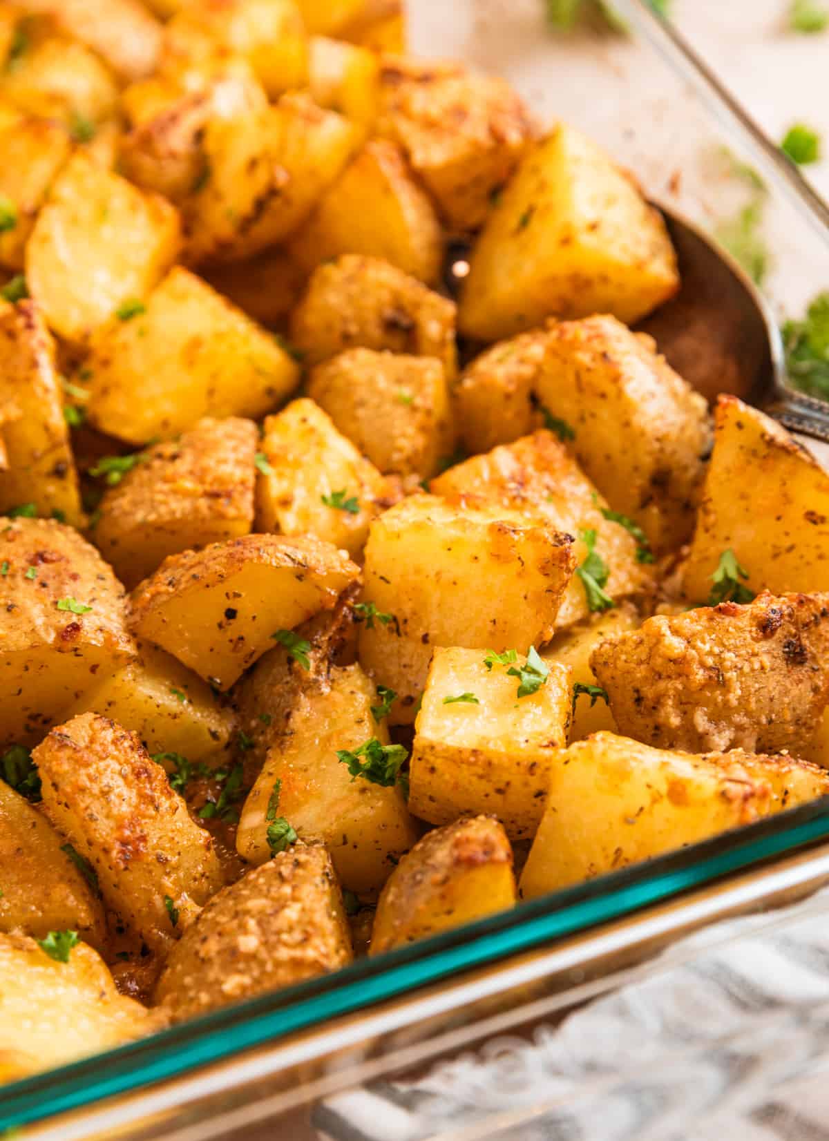 Potatoes in pan with serving spoon topped with chopped parsley.