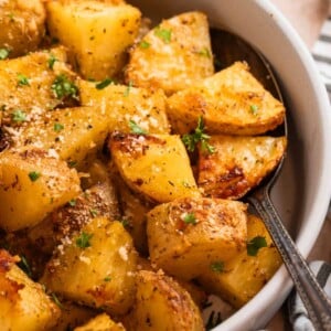 Parmesan roasted potatoes in serving dish with spoon topped with chopped fresh parsley and freshly grated parmesan.
