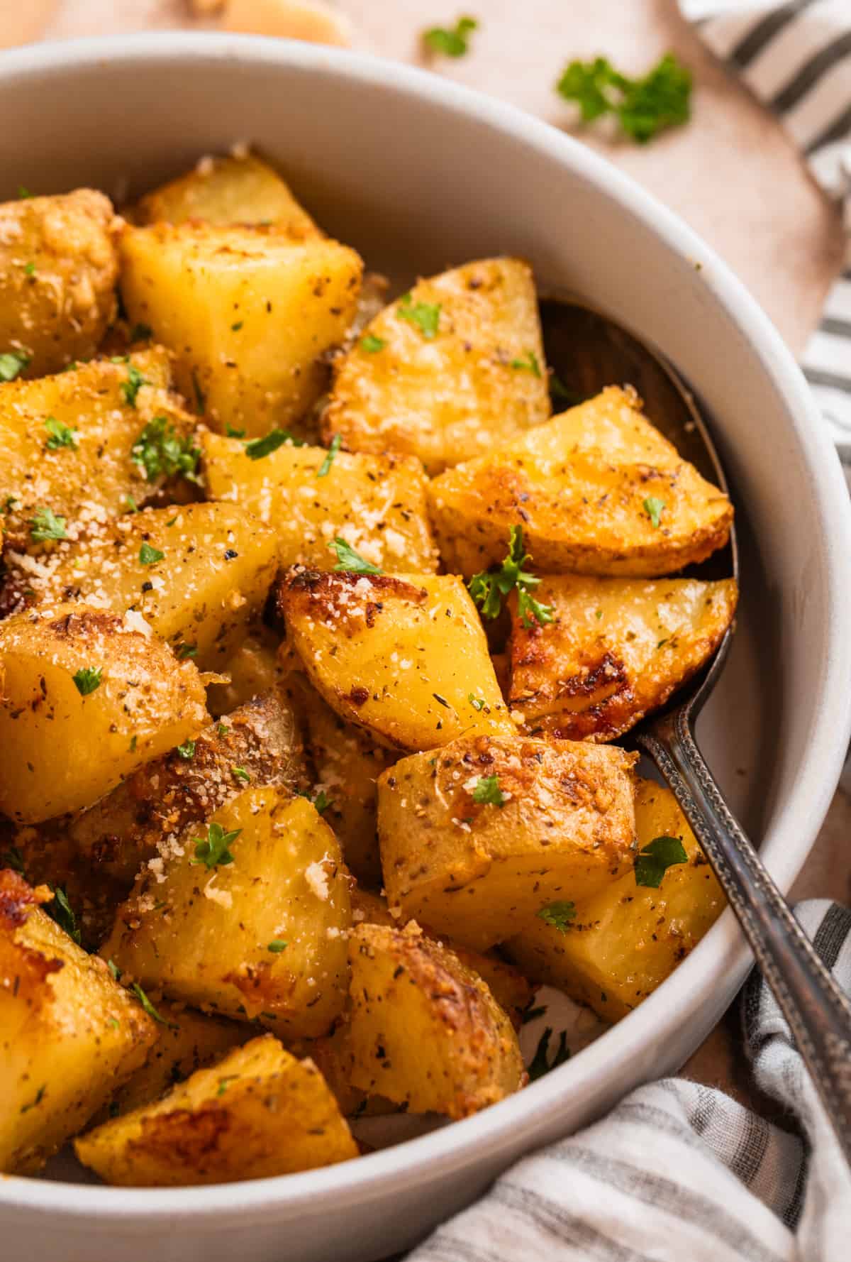 Parmesan crusted potatoes in serving bowl with freshly grated parmesan and chopped parsley on top.
