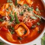 White bowl with tomato tortellini soup and spoon scooping in.