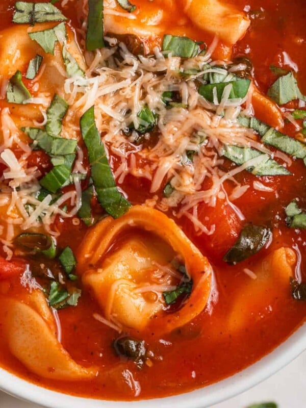 White bowl with tomato tortellini soup and spoon scooping in.
