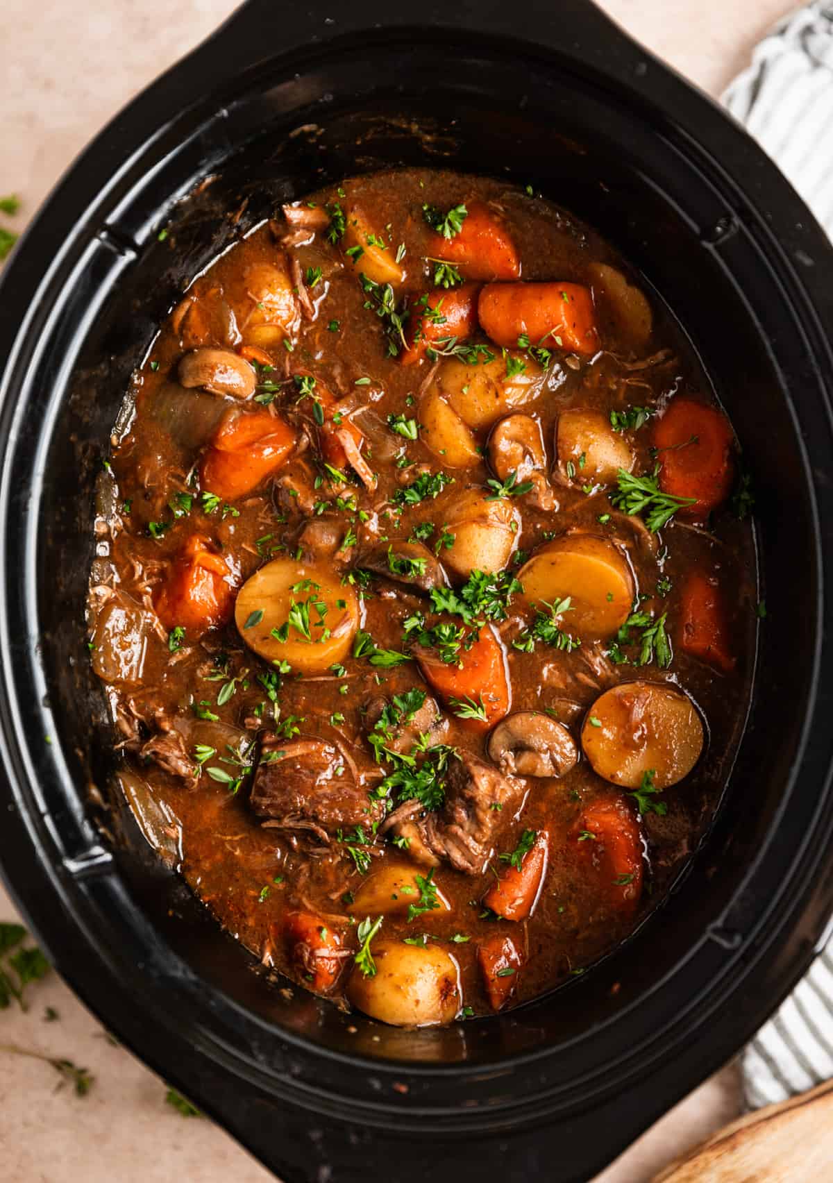 Beef and mushroom stew in slow cooker with potatoes and carrots and topped with parsley.