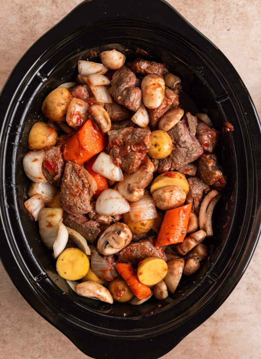 Slow cooker filled with beef mushroom stew ingredients.