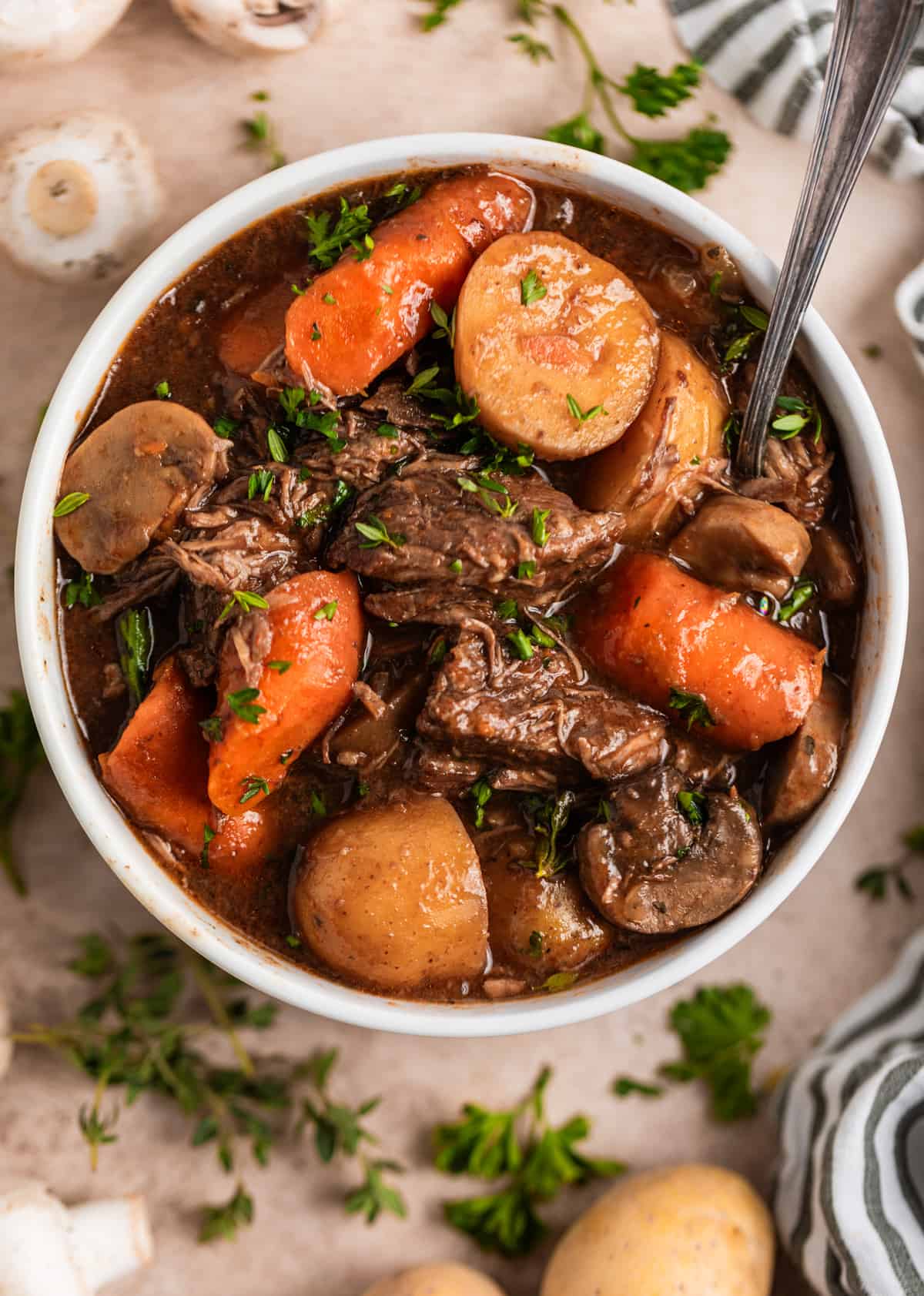 Overhead view of white bowl with mushroom beef stew with spoon.