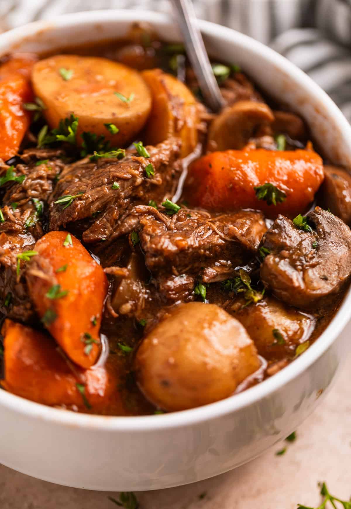 White dish with beef stew with potatoes, carrots, mushrooms and onion topped with parsley.