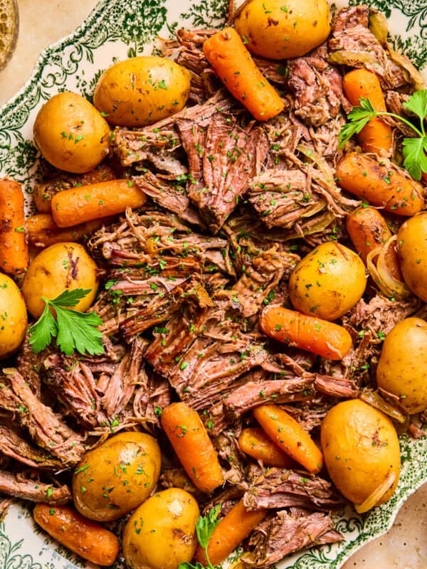 Plate with pot roast served with meat, potatoes and carrots and chopped parsley on top.