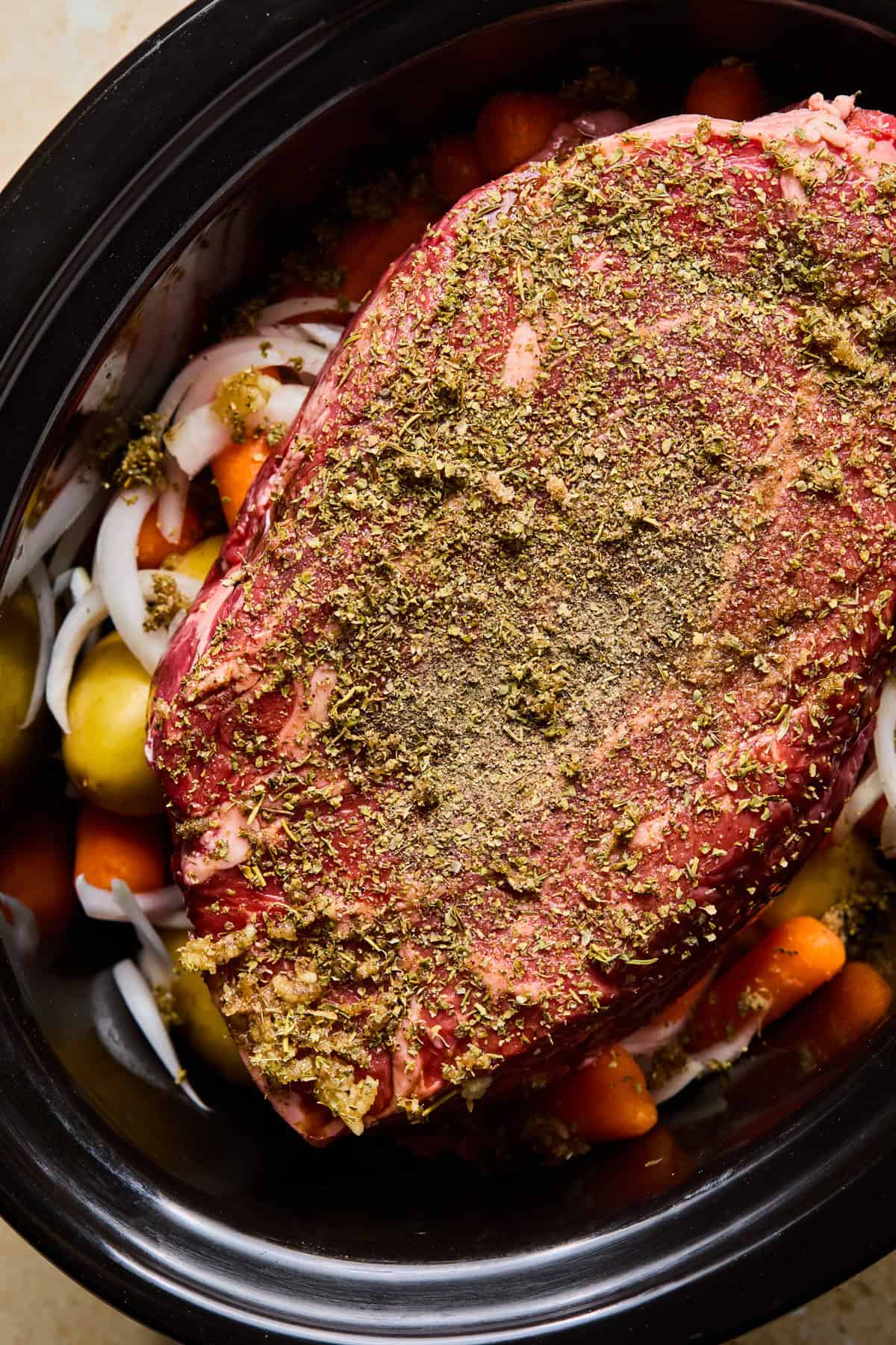 Chuck roast with herbs and seasoning on top of vegetables in crock pot before cooking.