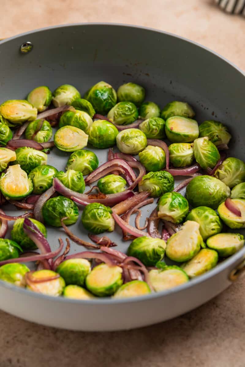 Brussels sprouts and red onion sautéed in skillet. 