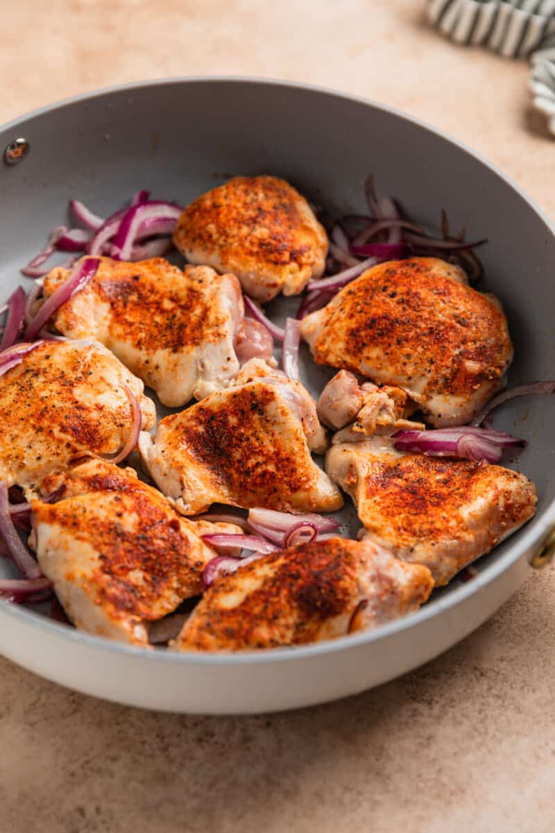 Seared chicken thighs and red onion in skillet.