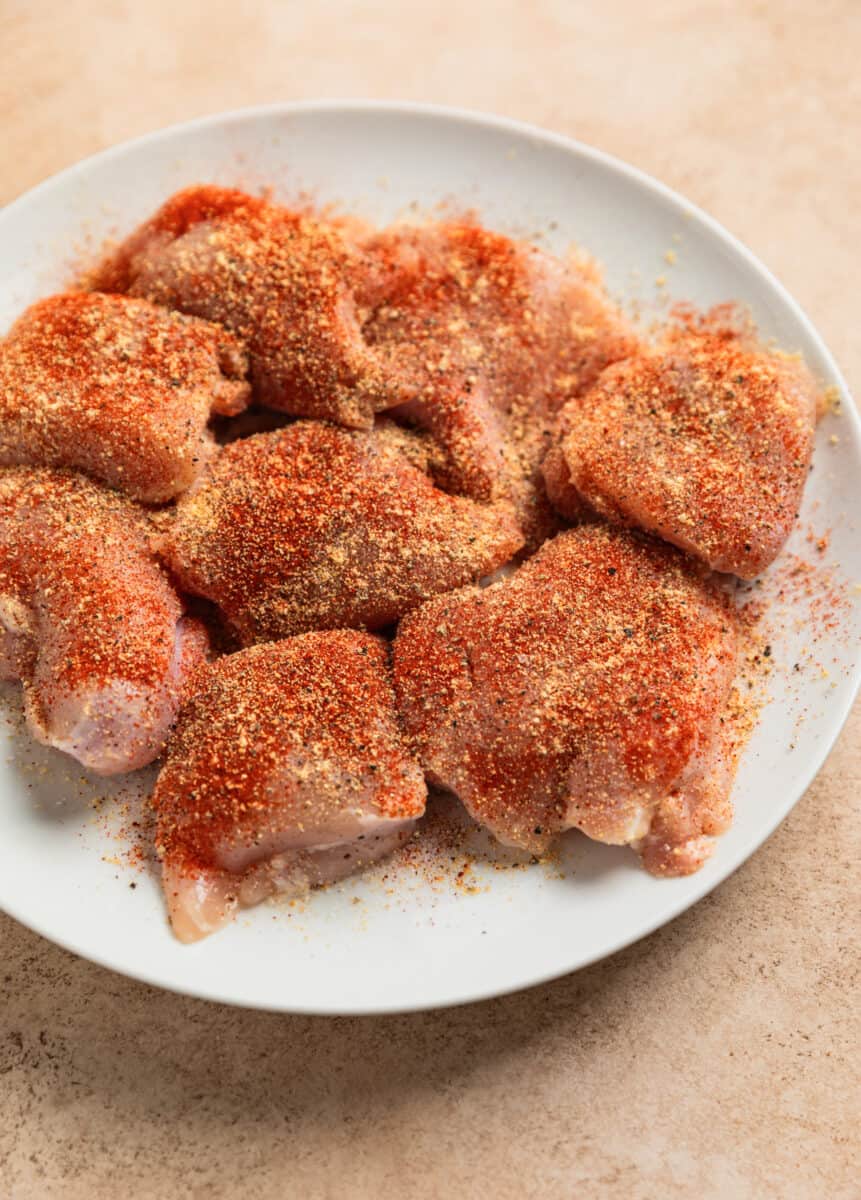 Seasoned chicken thighs on white plate before being cooked.