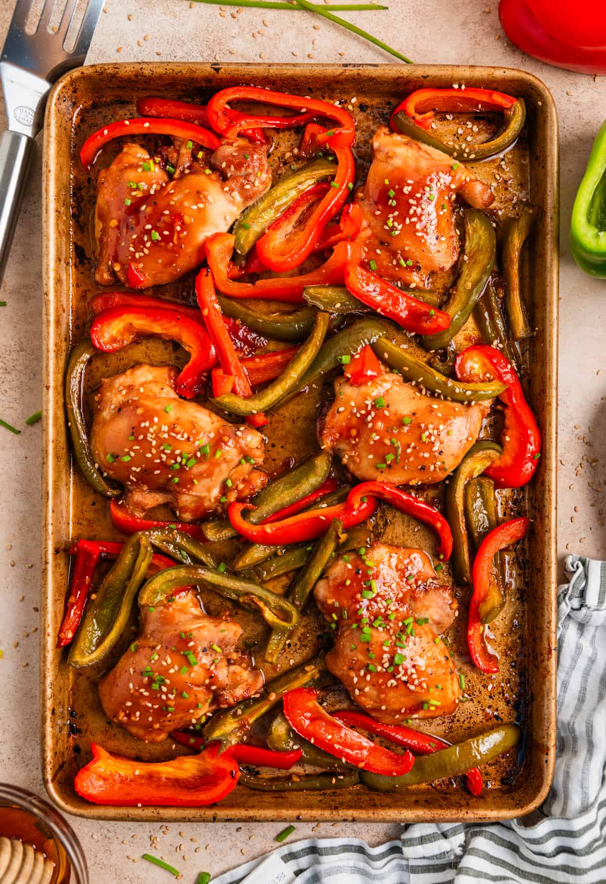 Chicken thighs and bell peppers on cookie sheet topped with sesame seeds and chives.