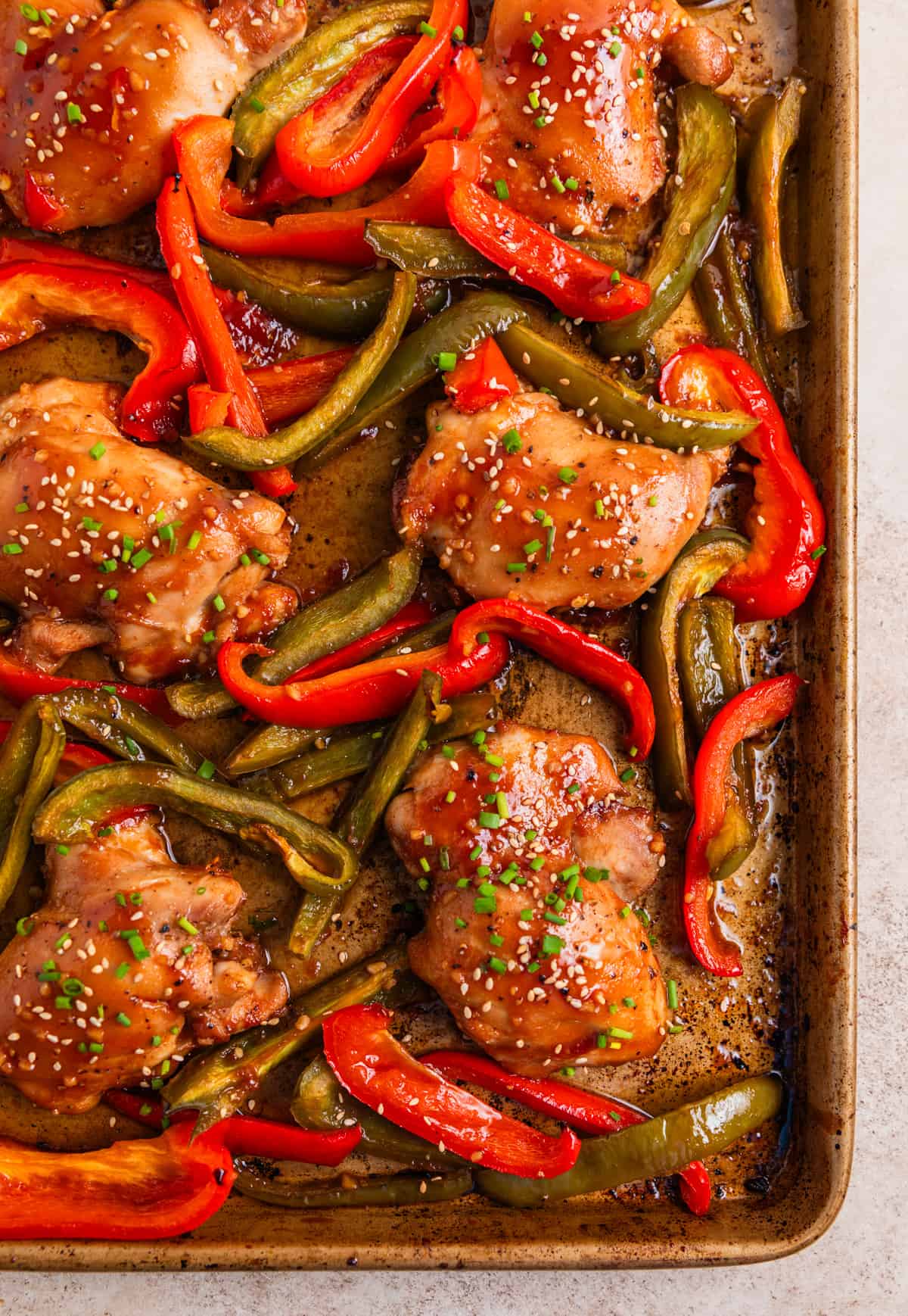 Chicken thighs and red and green bell peppers baked on sheet pan and topped with chives and sesame seeds.