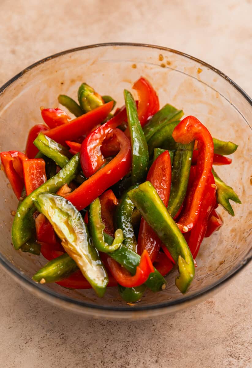 Bell peppers tossed with sauce in glass mixing bowl.