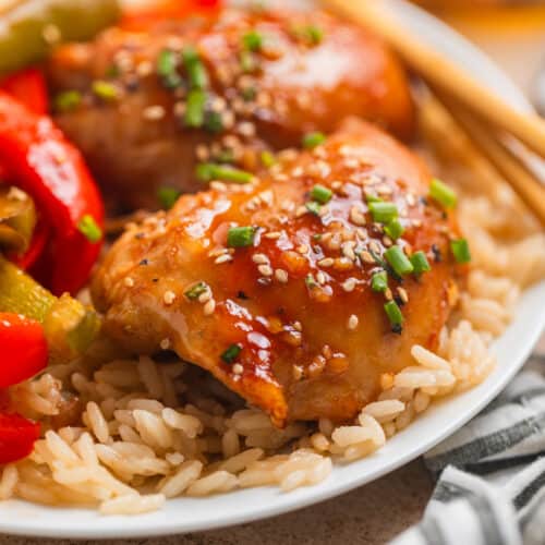 Honey garlic chicken thighs over rice with sliced bell peppers and chopsticks.