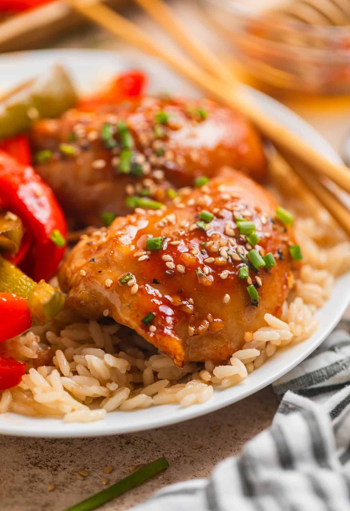 Honey garlic chicken thighs with peppers over rice on white plate.