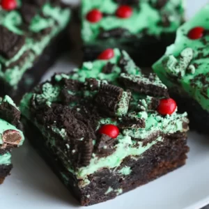 Green mint iced brownies with crushed Oreos and red candies on top.