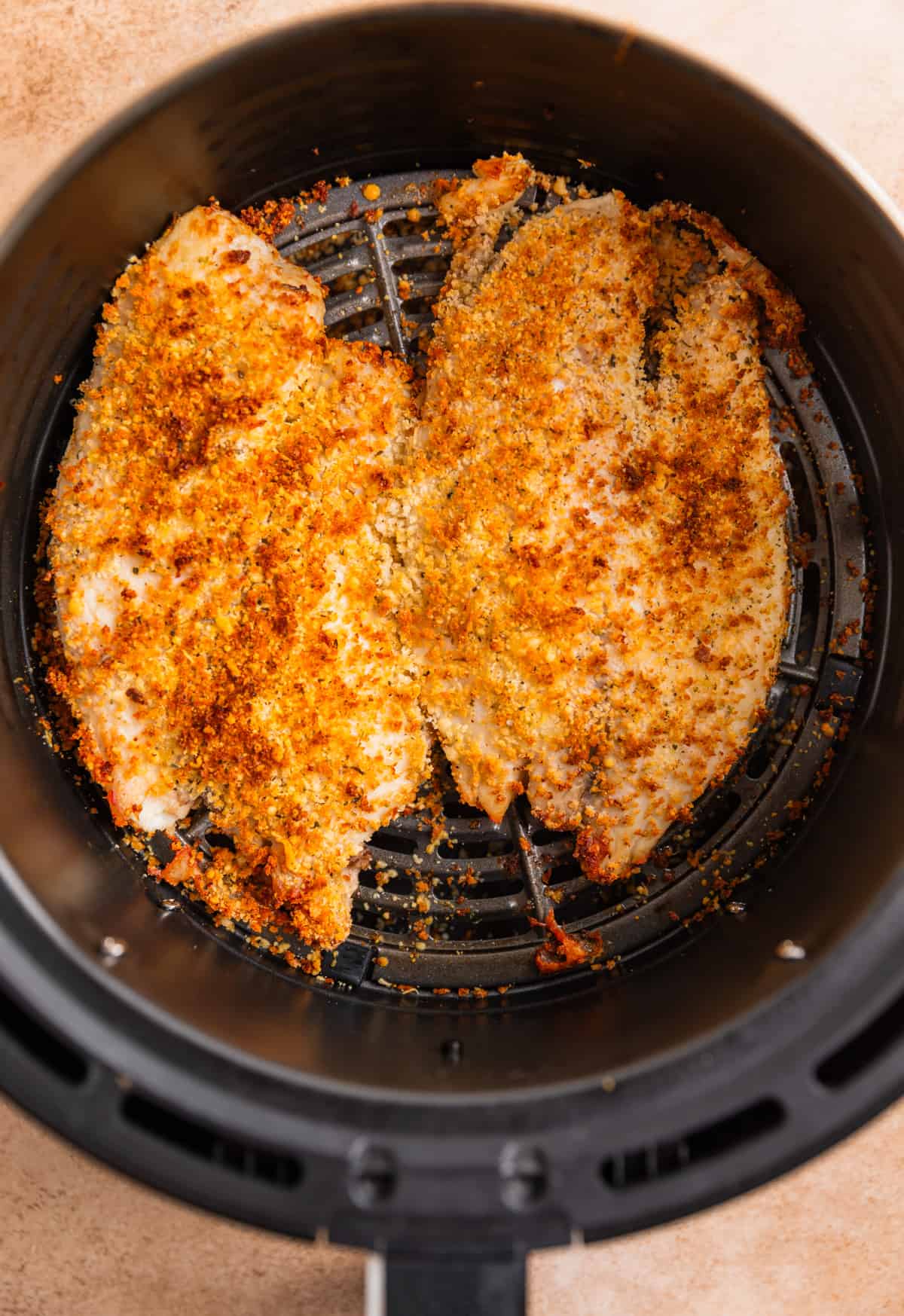 Parmesan crusted tilapia in air fryer basket after cooking.