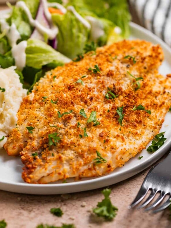 Air fryer parmesan crusted tilapia on white plate with salad and mashed potatoes.