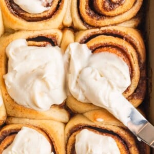 Buttermilk cinnamon rolls being iced with offset spatula.