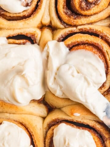 Buttermilk cinnamon rolls being iced with offset spatula.
