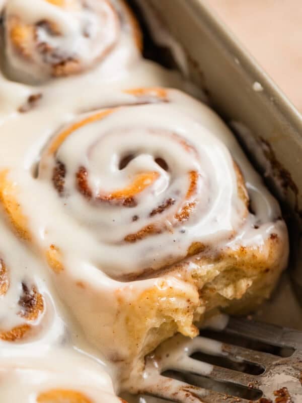 Iced buttermilk cinnamon rolls in pan with serving spatula.