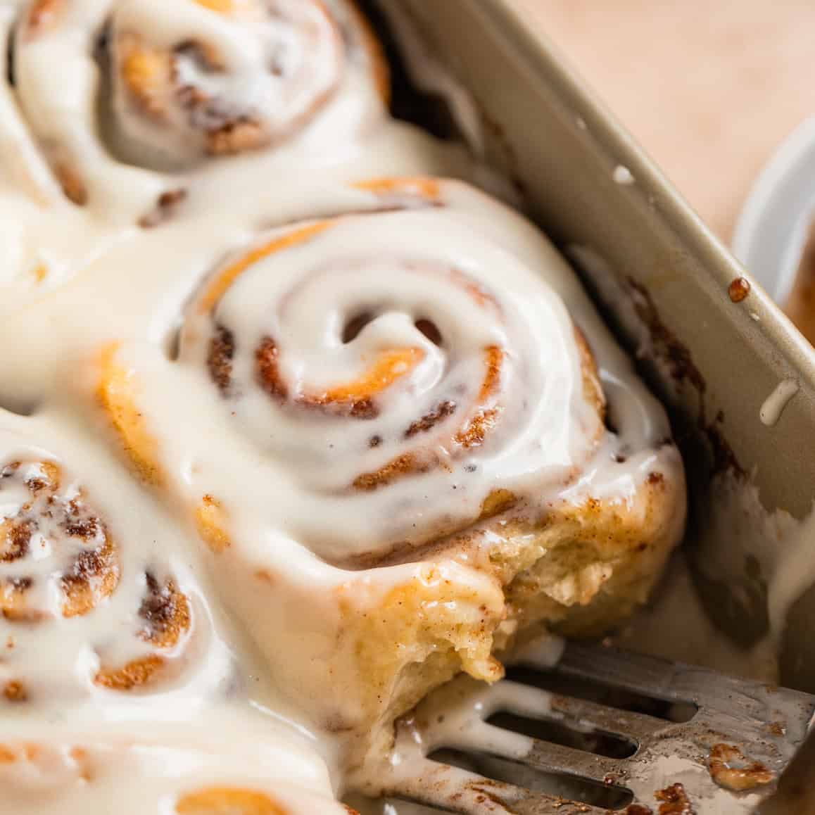 Iced buttermilk cinnamon rolls in pan with serving spatula.