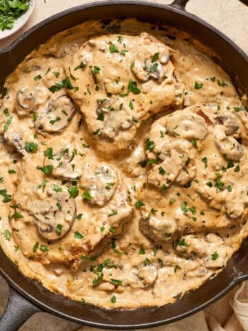 Skillet with cream of mushroom pork chops topped with chopped parsley.