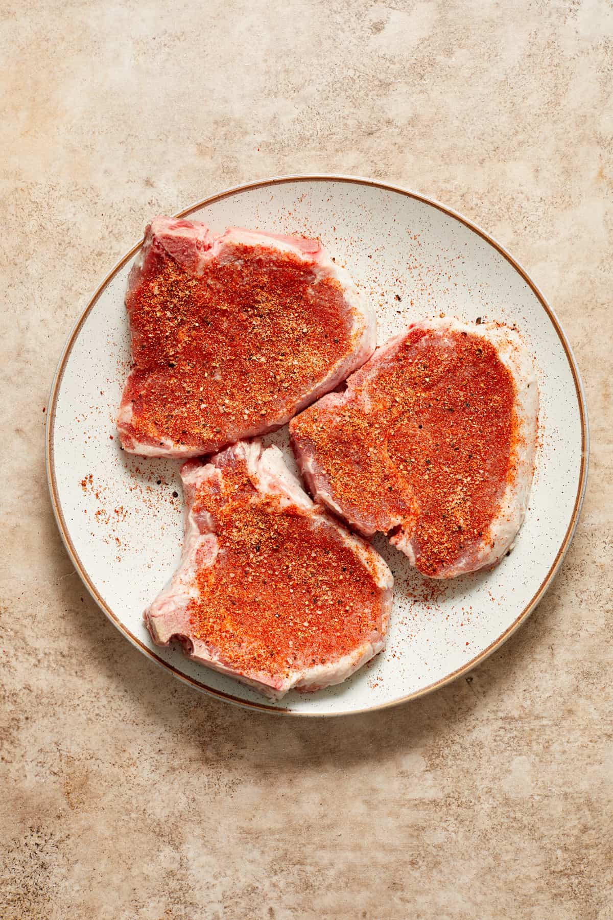 Pork chops with seasoning on white plate.