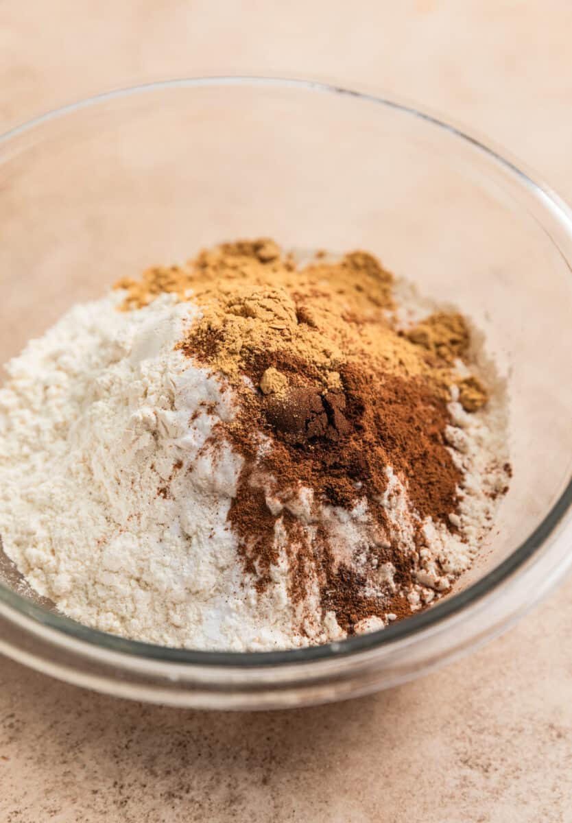Flour, cinnamon, ginger, cloves and baking soda in glass mixing bowl.