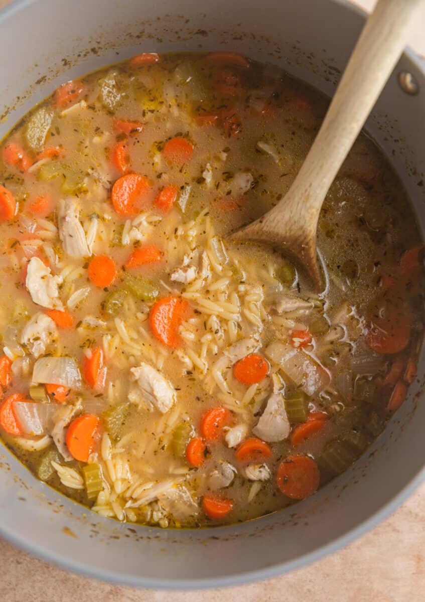 Chicken added to lemon chicken orzo soup with wooden spoon.