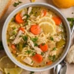 Bowl with orzo soup with chicken, carrots, celery and topped with lemon and parsley.