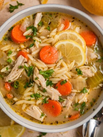 Bowl with orzo soup with chicken, carrots, celery and topped with lemon and parsley.