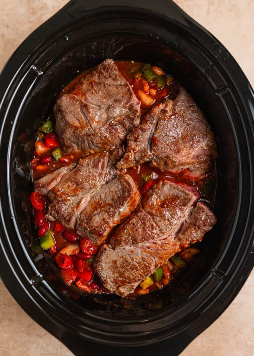 Seared chuck roast in slow cooker on top of chili ingredients.