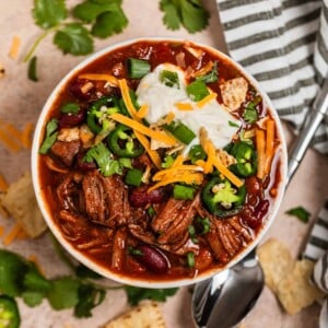 Overhead view of shredded beef chili topped with sour cream, cilantro, cheese and more.