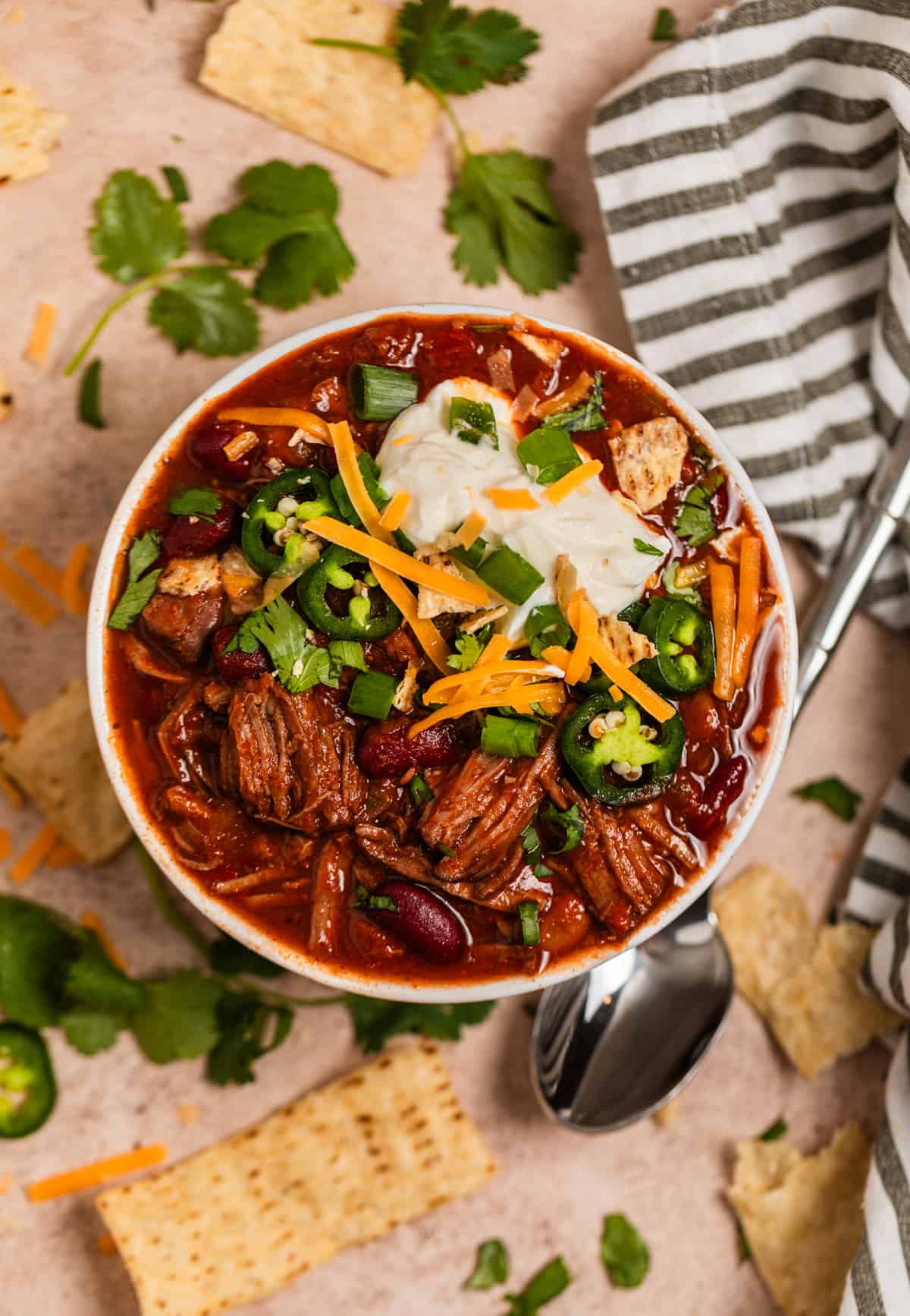 Overhead view of chili in bowl topped with sour cream, cheese, cilantro and other toppings.