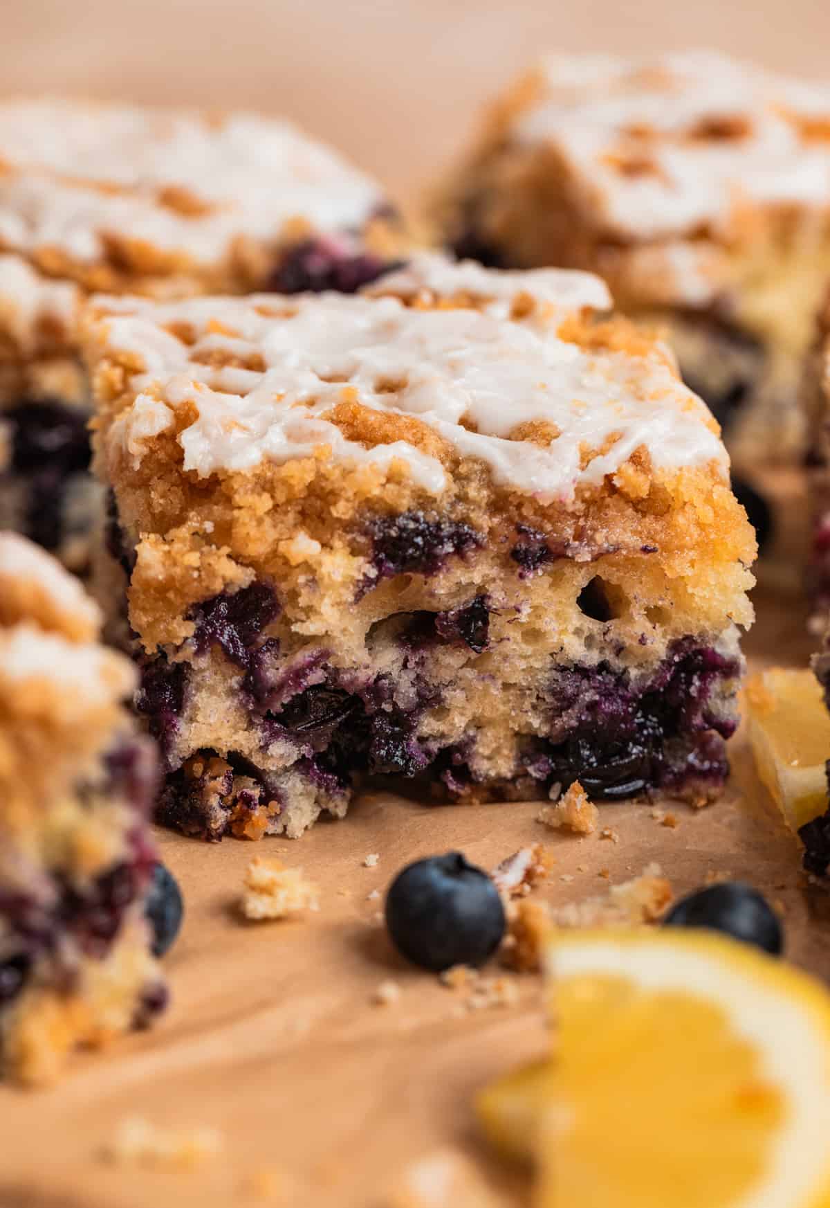 Slice of blueberry coffee cake with icing over top and lemons and fresh blueberries beside it.