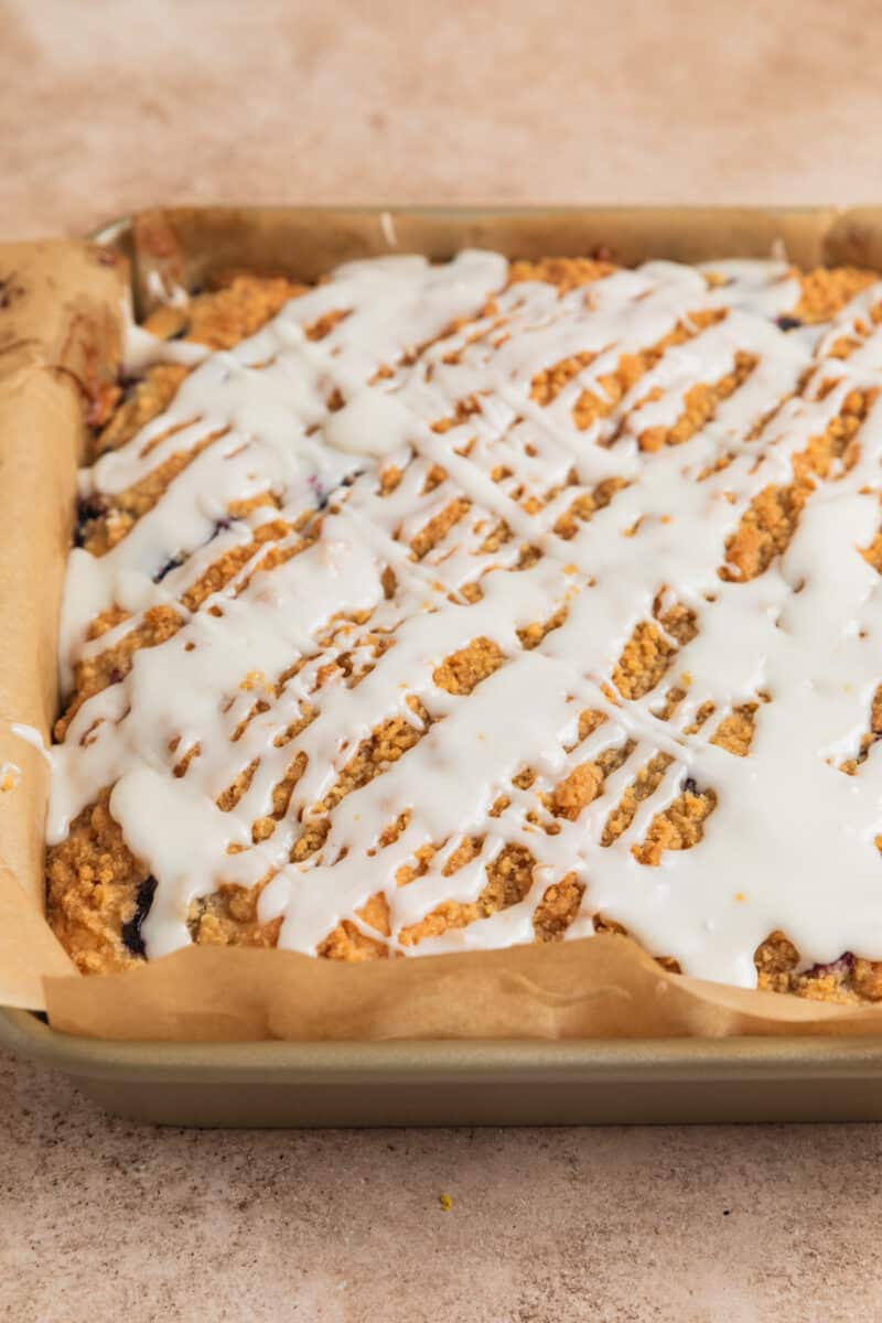 Icing drizzled over top of coffee cake in parchment lined pan.