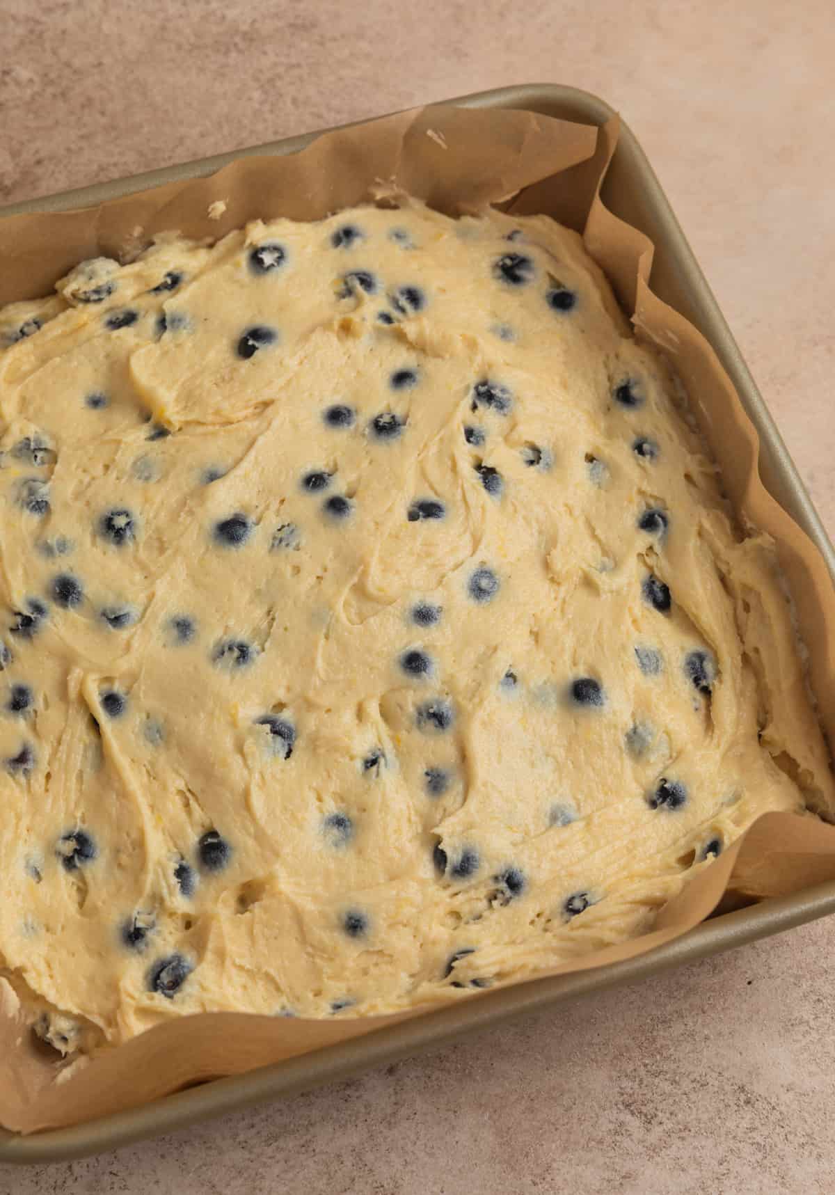 Parchment lined baking pan with lemon blueberry cake batter.