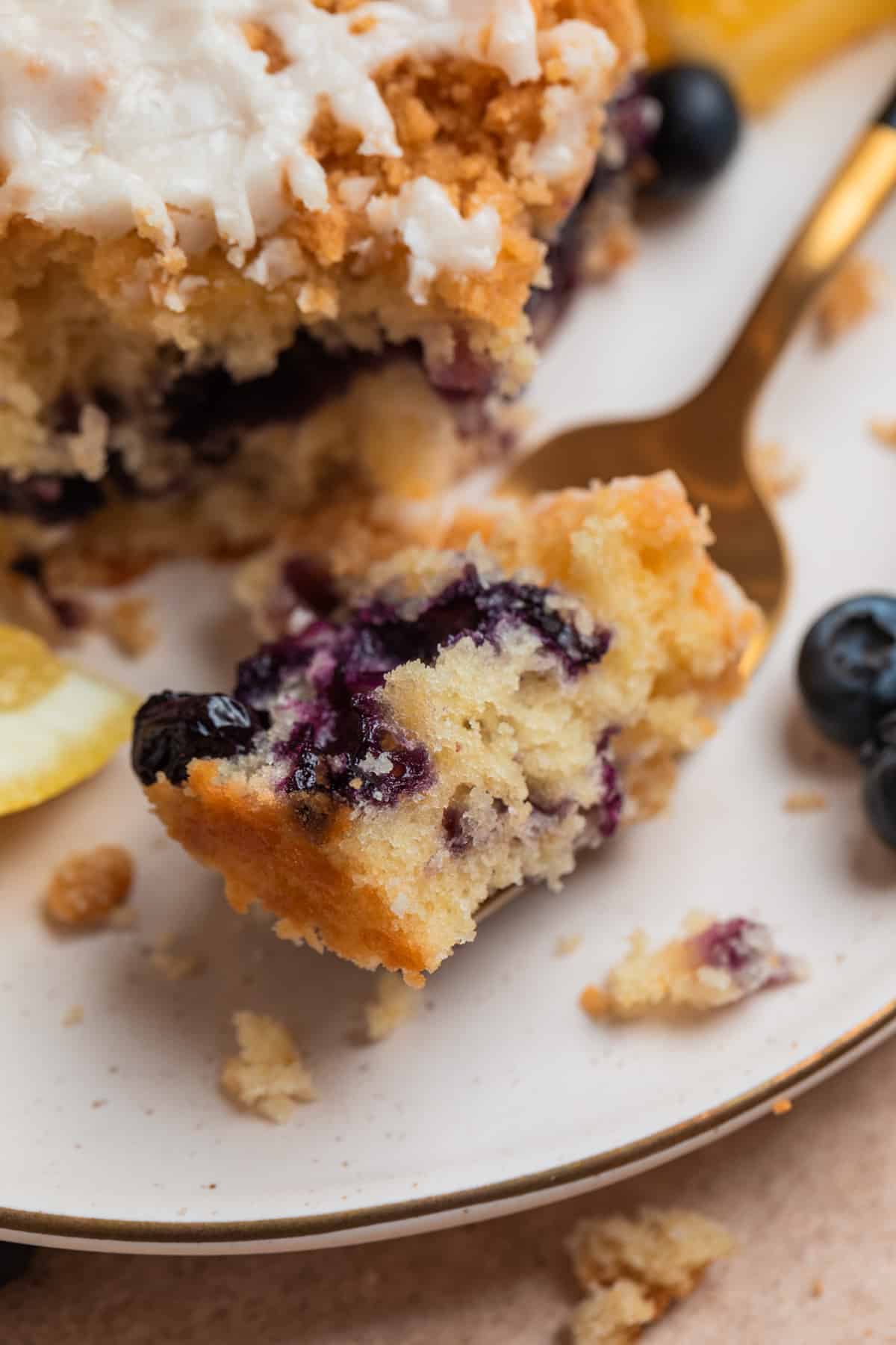 Forkful of lemon blueberry coffee cake on plate with slice of cake.